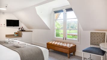 Un dormitorio con cama, un banco, una silla, un televisor y una ventana con vistas a zonas verdes.