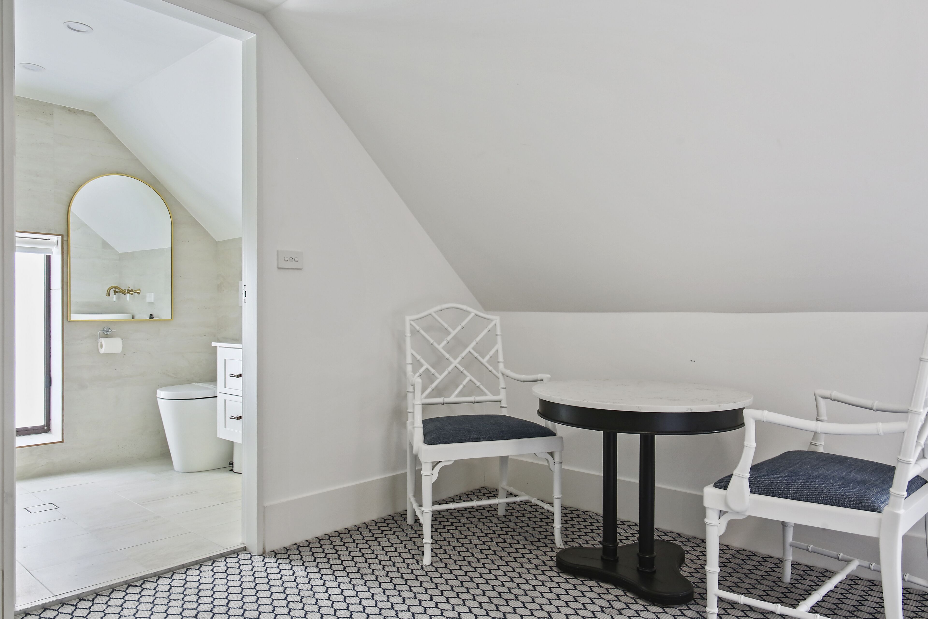 A small, white-walled room with a tiled floor, a round table, two white chairs, a white cabinet, and a mirror on the wall.