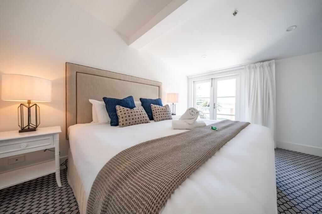 A hotel room with a large bed, a bedside table with a lamp, a window with curtains, and a patterned floor.