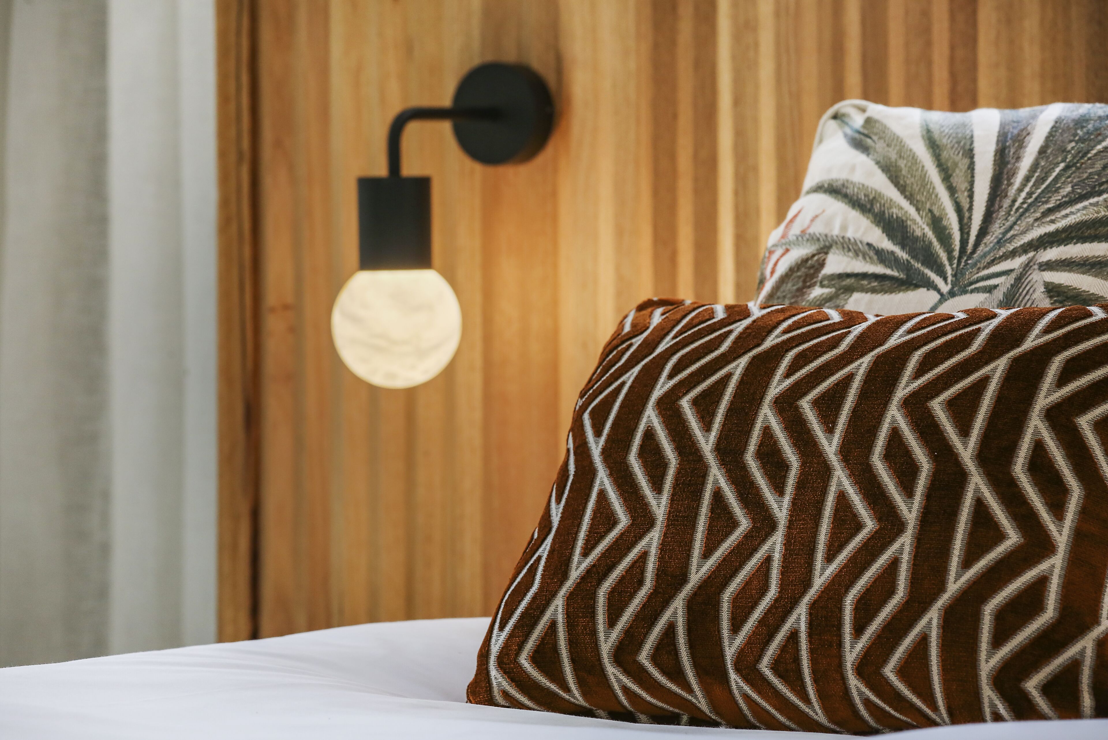 A bed with a patterned pillow and a wall-mounted light fixture.