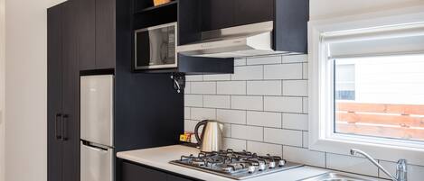 A modern kitchen with dark cabinetry, a stainless steel refrigerator, a gas stove, and a window with a view of a brick wall.