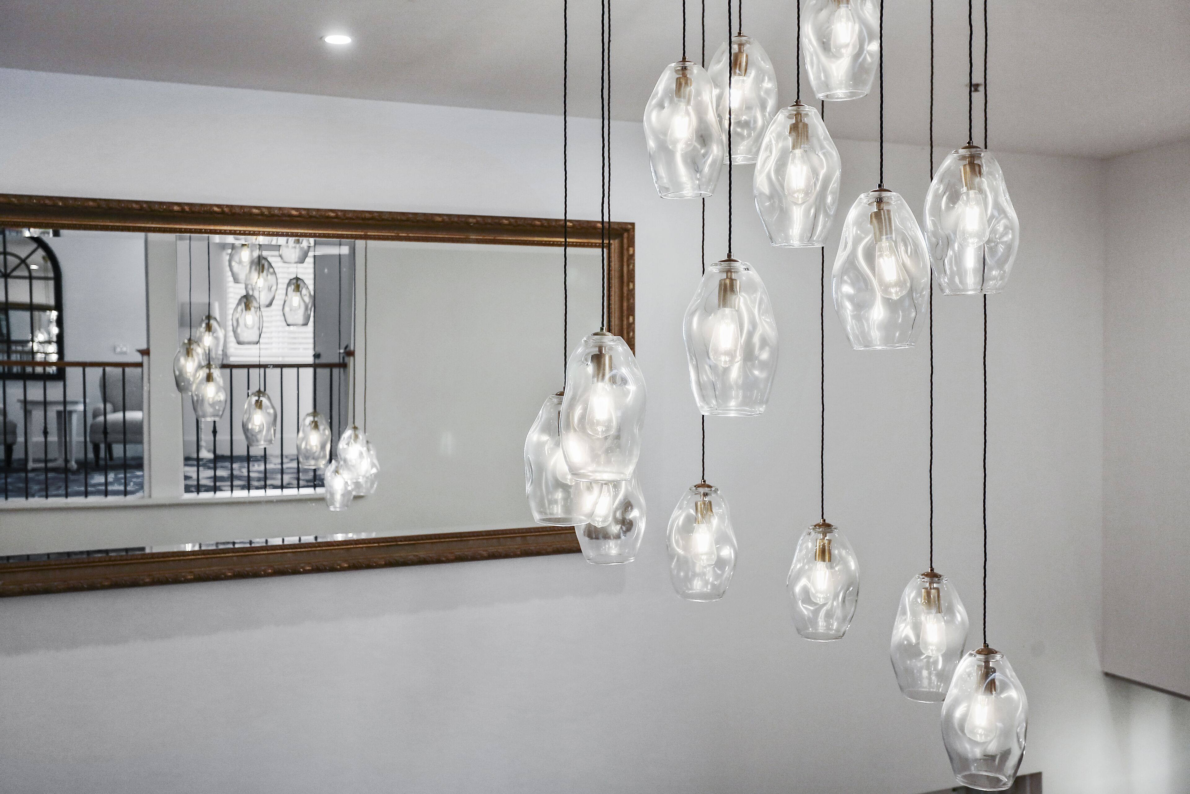 Un interior moderno con lámparas colgantes de cristal y un espejo grande que refleja una escalera.