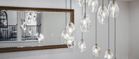 Un interior moderno con lámparas colgantes de cristal y un espejo grande que refleja una escalera.