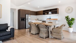 A modern kitchen with a dining area, featuring a wooden table, wicker chairs, and built-in wooden cabinets. - Seahorse Inn Hotel & Villas (Boydtown)