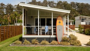 A modern building with a covered porch, a surfboard leaning against the wall, and a wooden fence in the background. - Seahorse Inn Hotel & Villas (Boydtown)