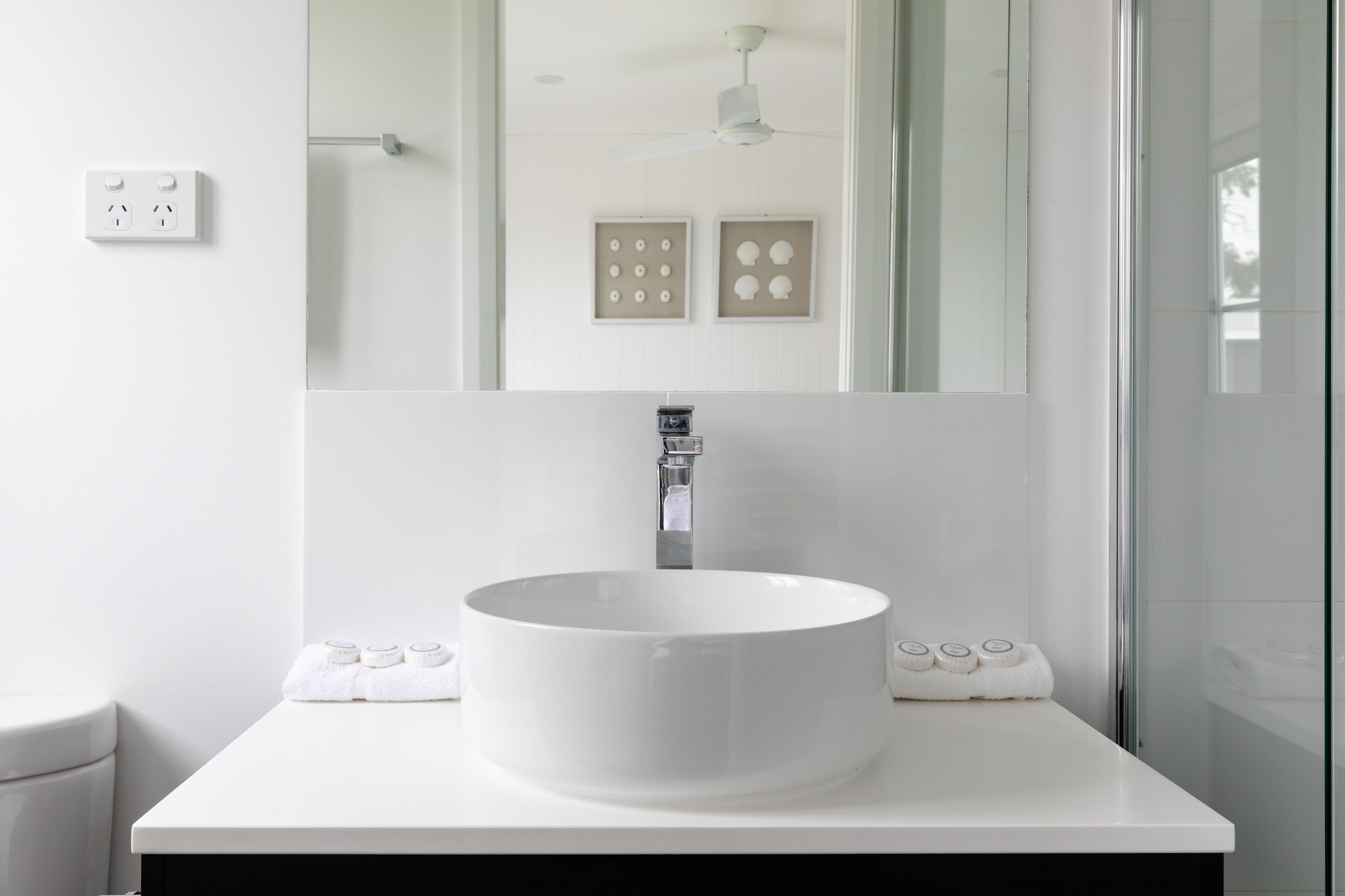 Une salle de bain moderne avec un lavabo blanc, un miroir et un ventilateur de plafond.