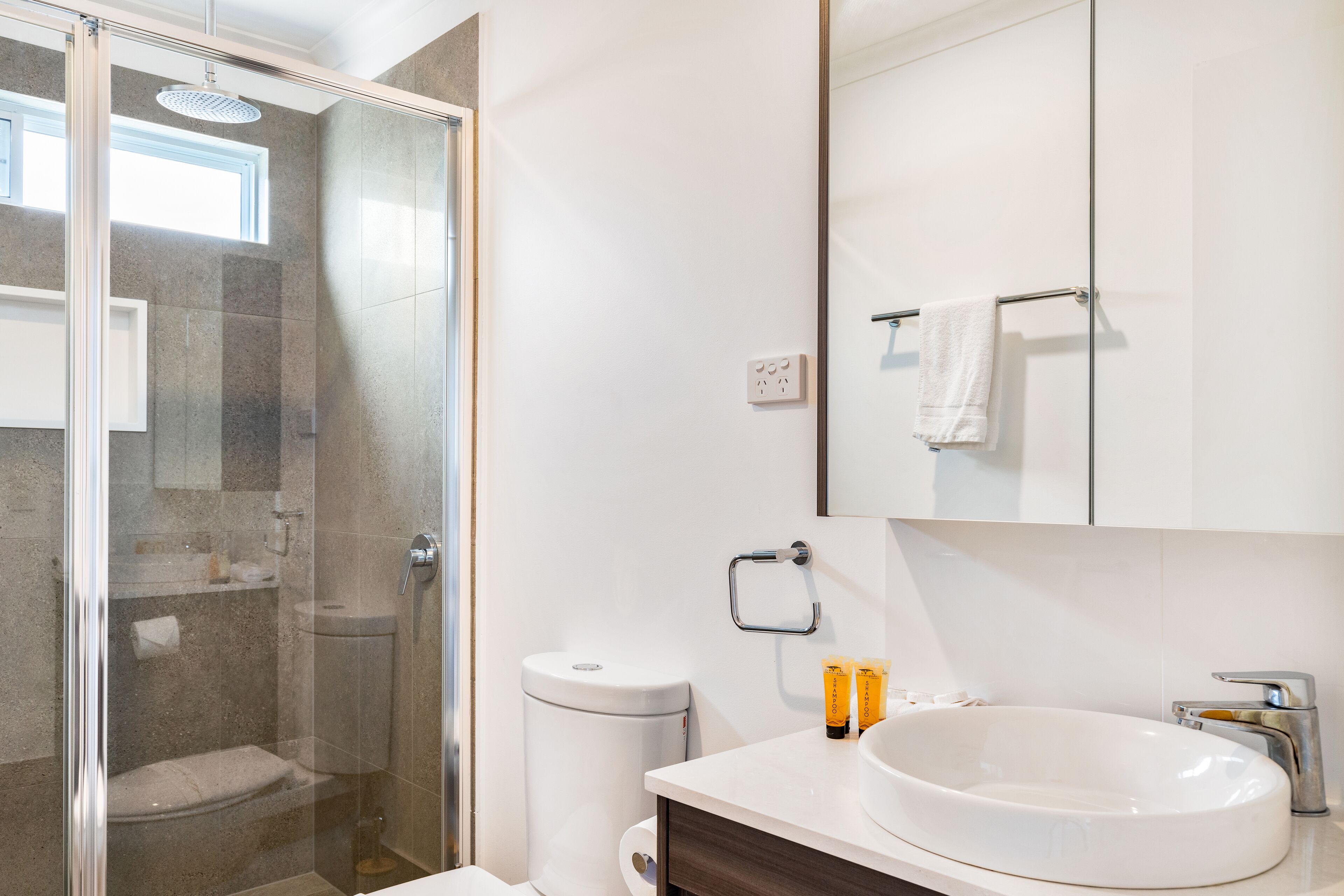 A modern bathroom with a glass-enclosed shower, a white sink, and a large mirror above the vanity.