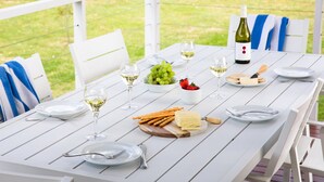 A white wooden table set for a meal with plates, cutlery, a bottle of white wine, grapes, cheese, and crackers.