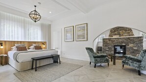 A bedroom with a large bed, a stone fireplace, and two armchairs.