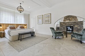A bedroom with a large bed, a stone fireplace, and two armchairs.