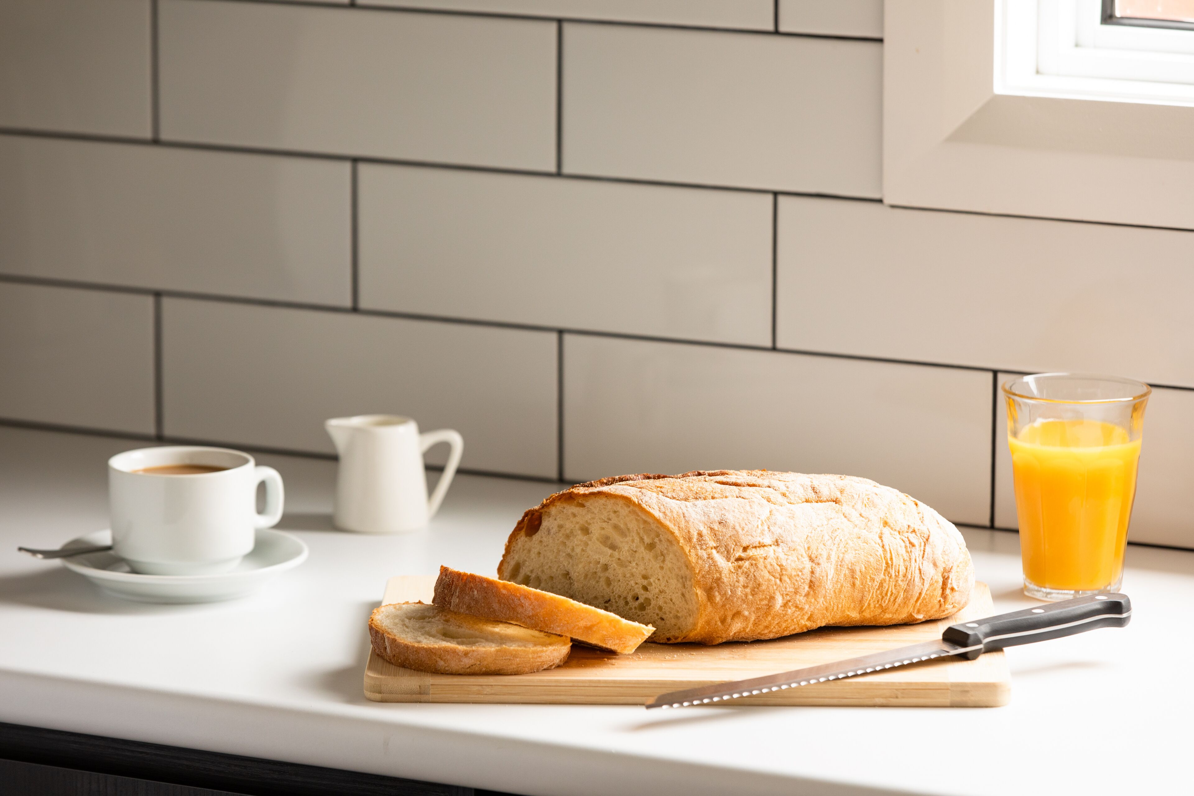 Ein Brot, ein Glas Orangensaft und eine Tasse Kaffee auf einer Küchenarbeitsplatte.