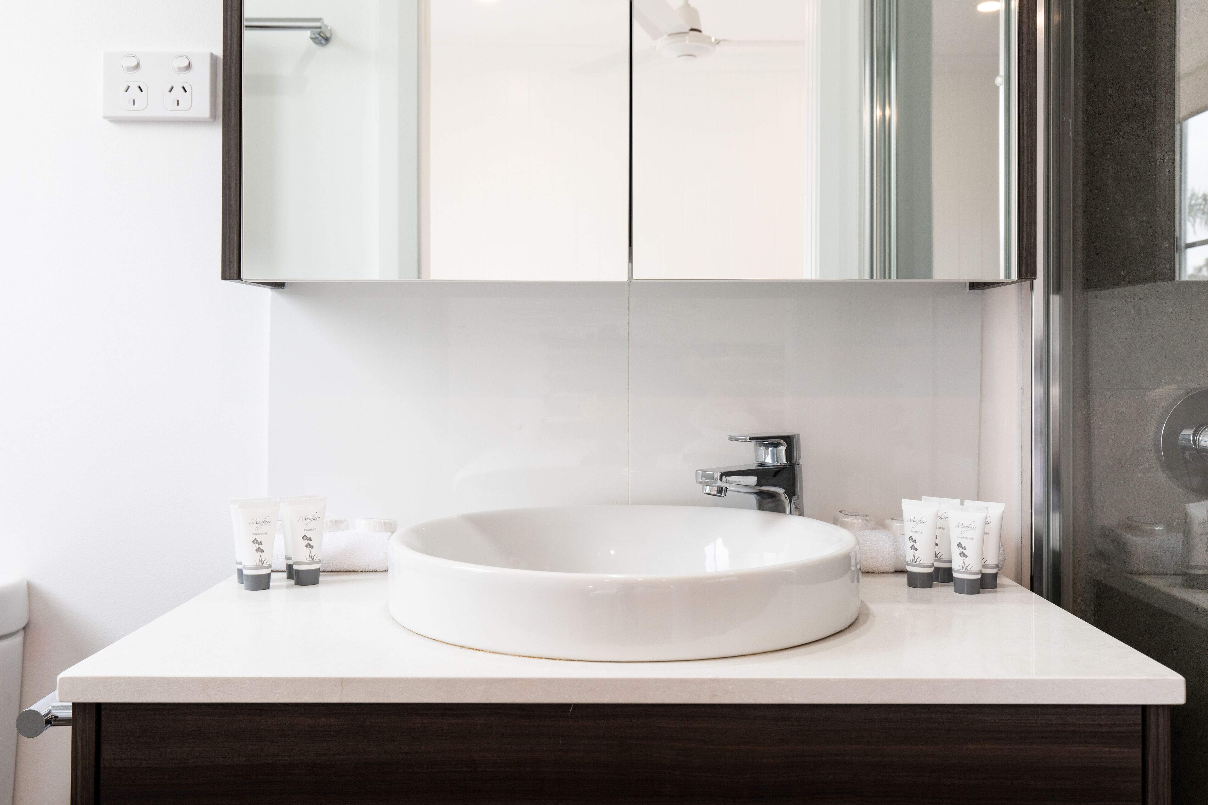 A modern bathroom with a white sink, a mirror, and toiletries on the counter.