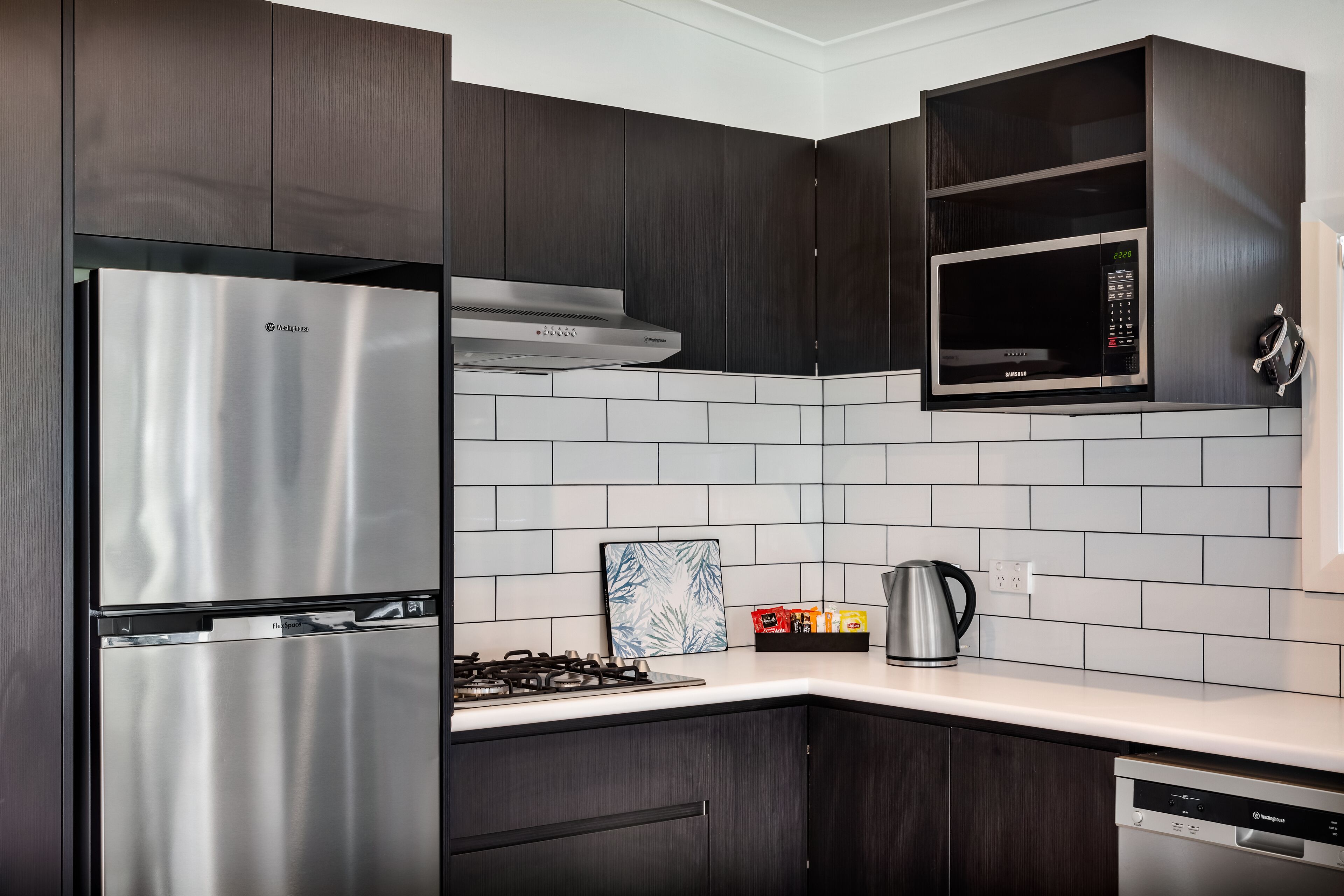 A modern kitchen with dark wood cabinets, a stainless steel refrigerator, a microwave, and a gas stove.