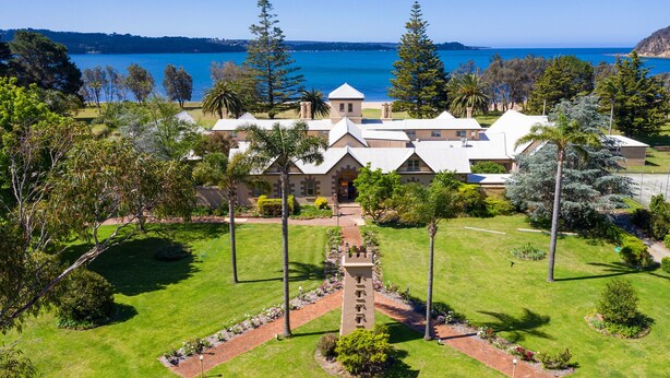 A large building with multiple sections, surrounded by well-maintained lawns and trees, with a view of a body of water in the background. - Seahorse Inn Hotel & Villas (Boydtown)