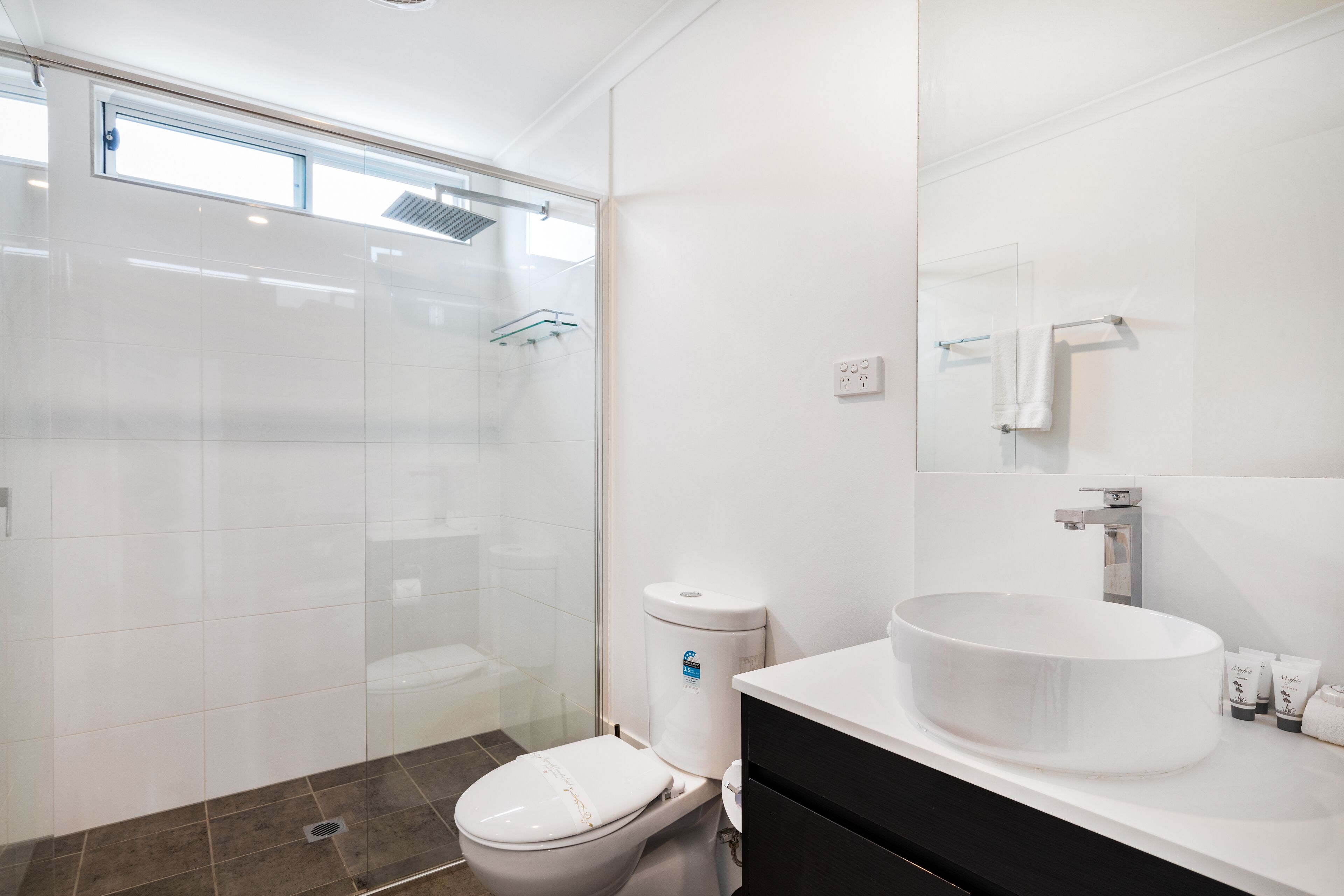A modern bathroom with a glass shower enclosure, a white toilet, a large white sink, and a black vanity.