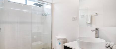 A modern bathroom with a glass shower enclosure, a white toilet, a large white sink, and a black vanity.