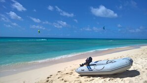 A beach with a white inflatable boat on the sand, clear turquoise water, and a few people in the distance. - Dreamcatcher Beachsides Apartments (Port Douglas)