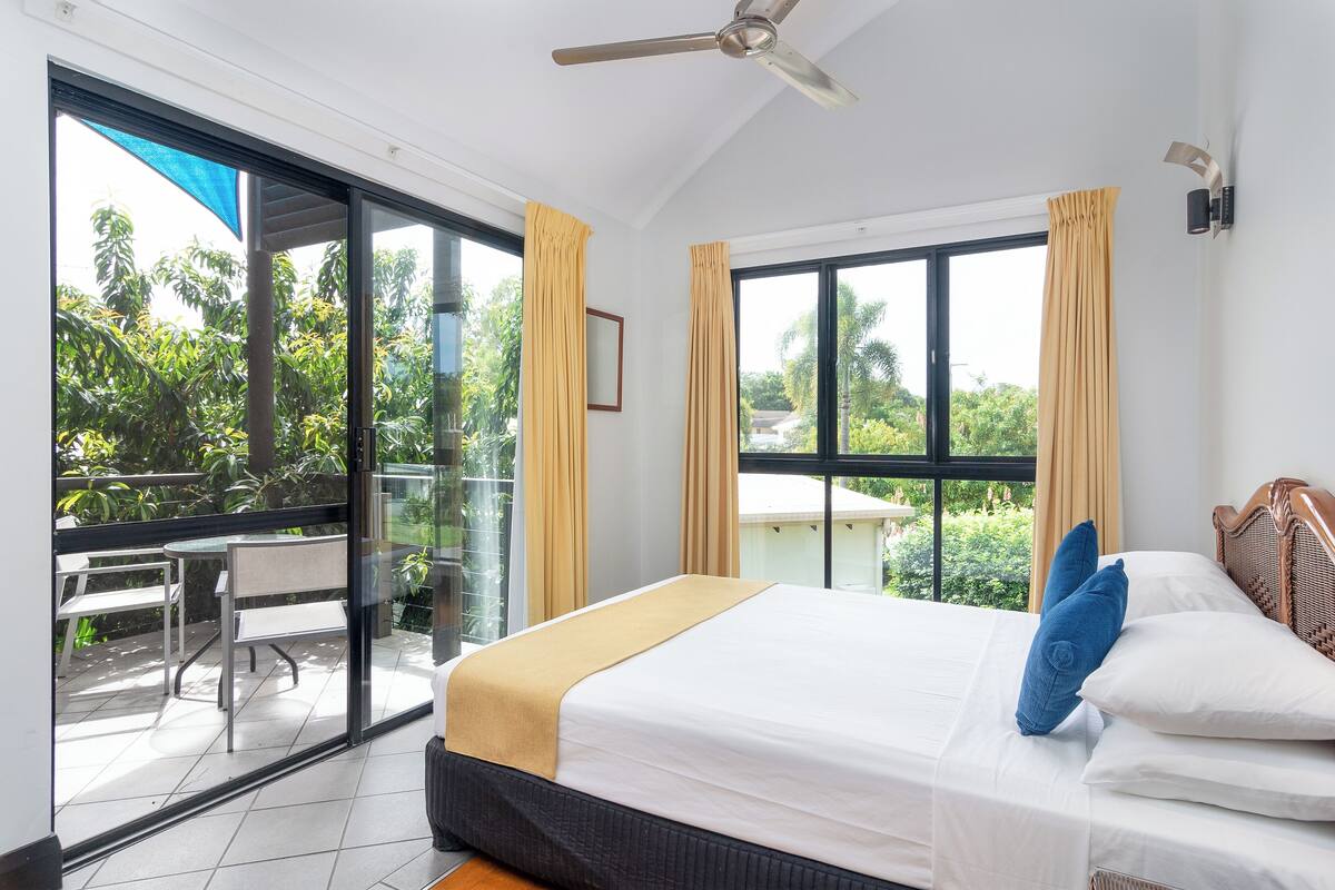 A hotel room with a bed, a ceiling fan, and large windows with curtains.