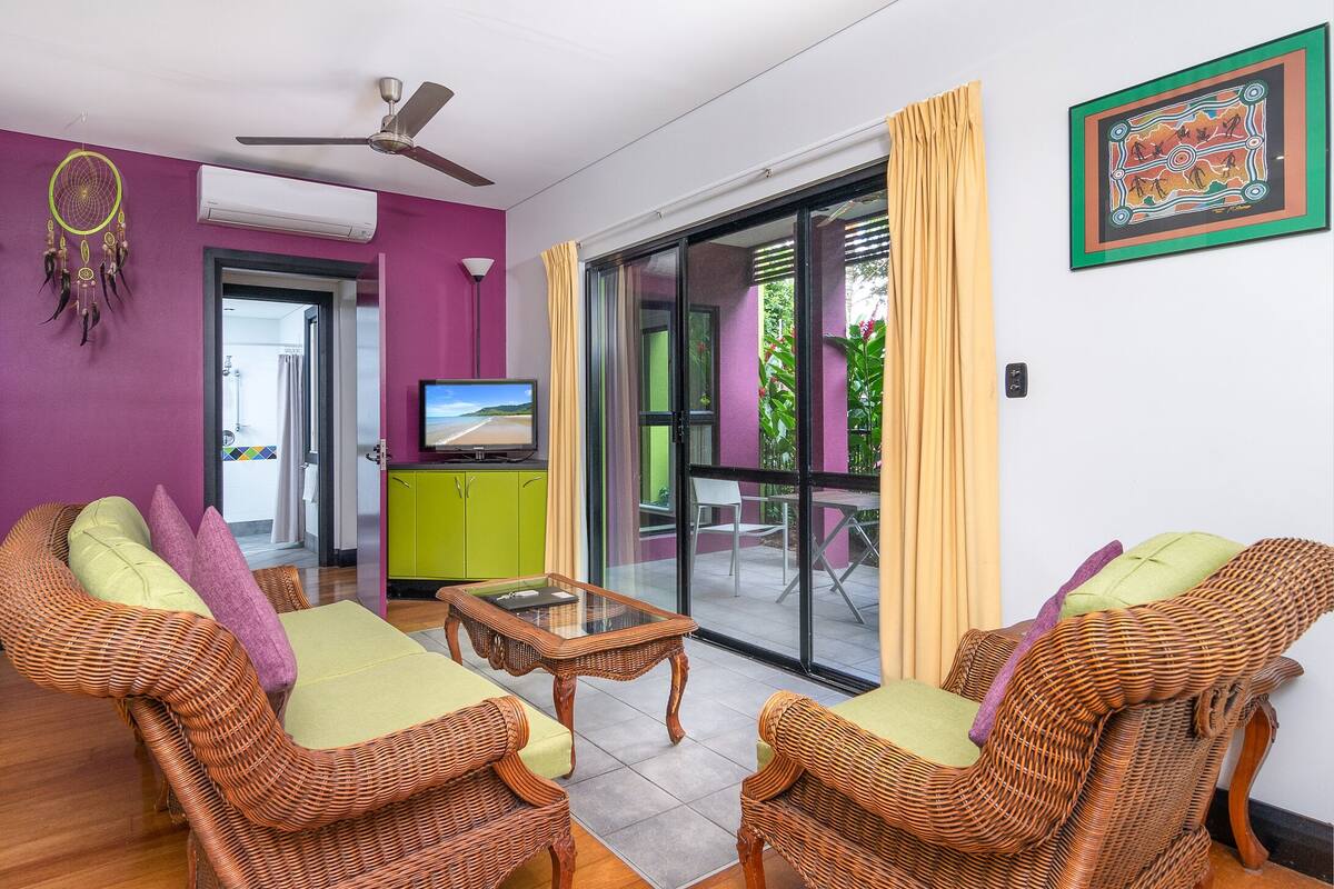 A room with wicker furniture, a television, and a sliding glass door leading to an outdoor area.