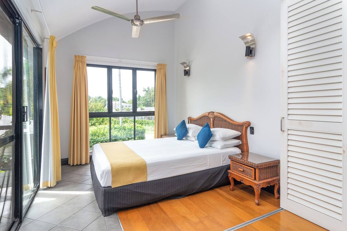 A bedroom with a bed, a nightstand, a ceiling fan, and a window with curtains.