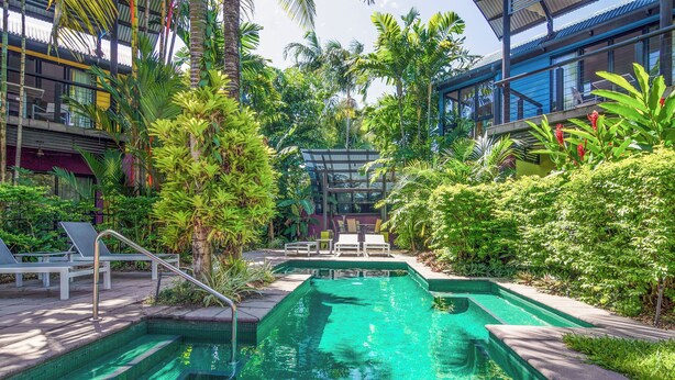 A swimming pool with steps, surrounded by lush greenery and modern buildings. - Dreamcatcher Beachsides Apartments (Port Douglas)