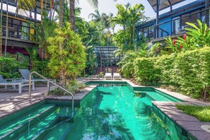 Ein Schwimmbecken mit Stufen, umgeben von üppiger Vegetation und modernen Gebäuden.