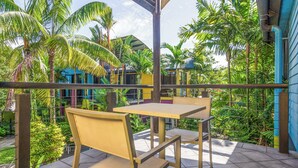 A terrace with two wooden tables and chairs, surrounded by lush greenery and palm trees. - Dreamcatcher Beachsides Apartments (Port Douglas)