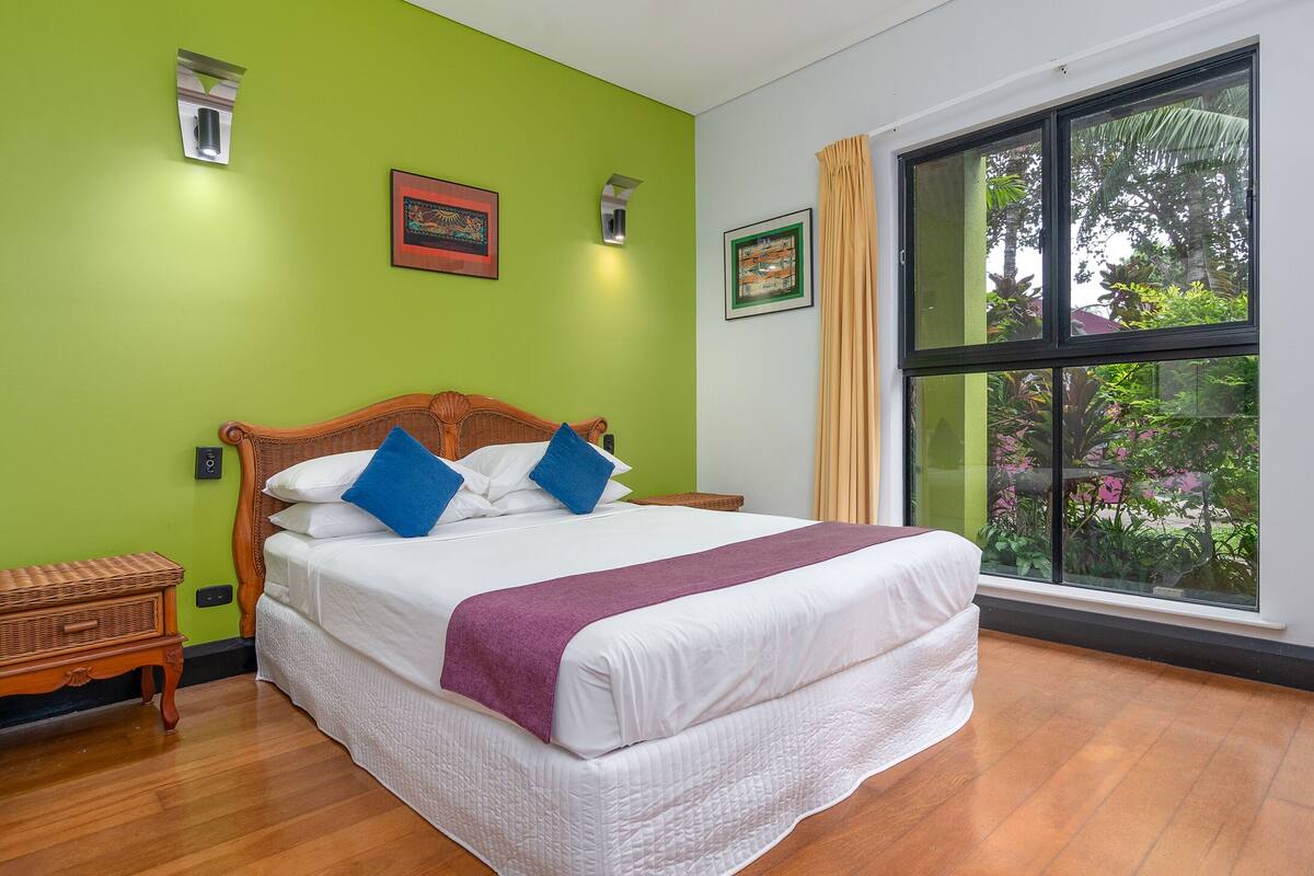 A bedroom with a large bed, green walls, and a window with a view of greenery.