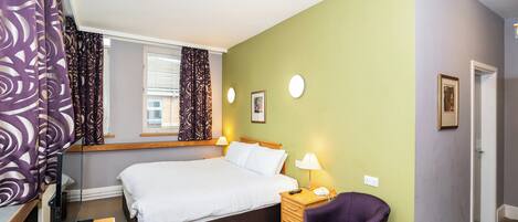 Quarto com cama, mesa de cabeceira, cadeira, janela e cortinas.
