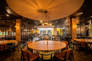 Un restaurante con mesas y sillas redondas, una zona de bar central y un diseño de techo moderno.