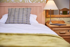 Una cama bien hecha con un cojín estampado, una lámpara de noche y una mesita de noche de madera con un cajón.