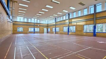 Un gimnasio interior amplio con techos altos, varias ventanas y una cancha de baloncesto.