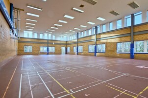 Un gimnasio interior amplio con techos altos, varias ventanas y una cancha de baloncesto.