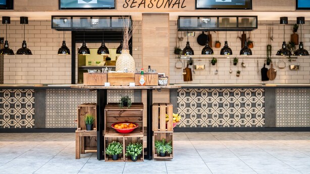 L'intérieur d'un restaurant, avec une enseigne indiquant « SAISON », des tables en bois, des plantes en pot et un mur recouvert de carreaux.