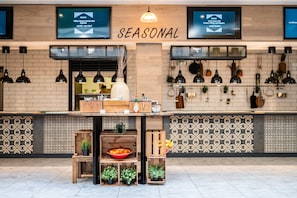 L'intérieur d'un restaurant, avec une enseigne indiquant « SAISON », des tables en bois, des plantes en pot et un mur recouvert de carreaux.