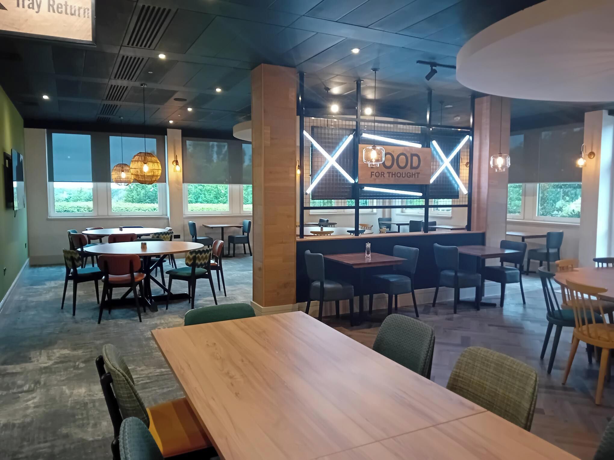 Et moderne spiseområde med runde borde og stole, et barområde og store vinduer med udsigt til grønne områder.