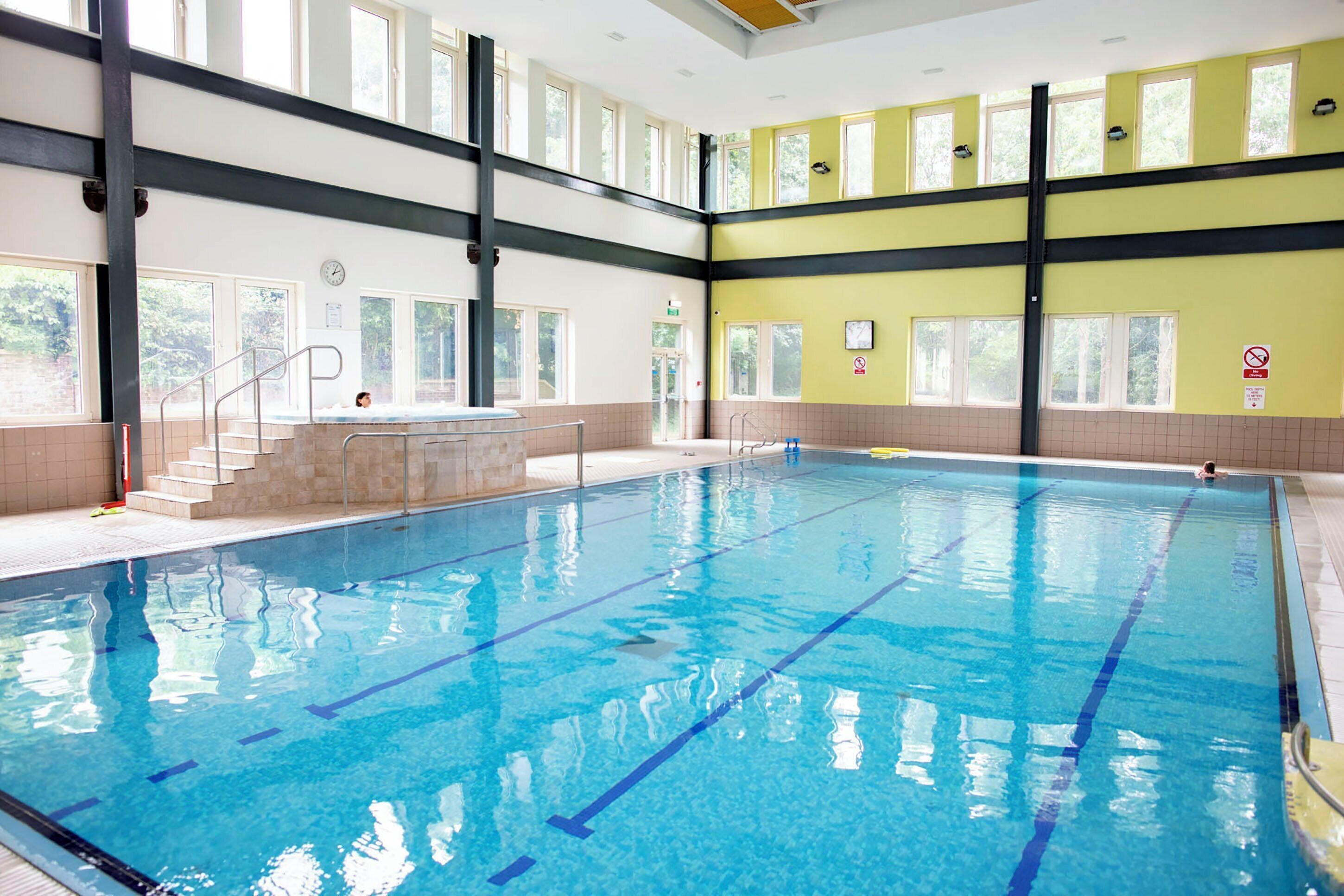 An indoor swimming pool with clear blue water, marked lanes, and a staircase leading to a higher level.