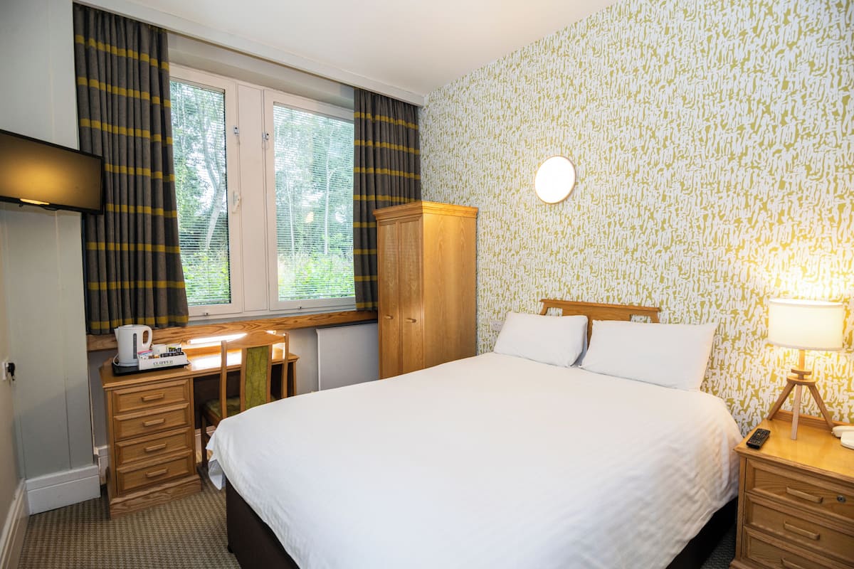 Une chambre d’hôtel avec un lit, un bureau avec un ordinateur, une armoire et une fenêtre avec des rideaux.