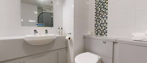 Un baño moderno con un lavamanos, espejo y retrete blancos.