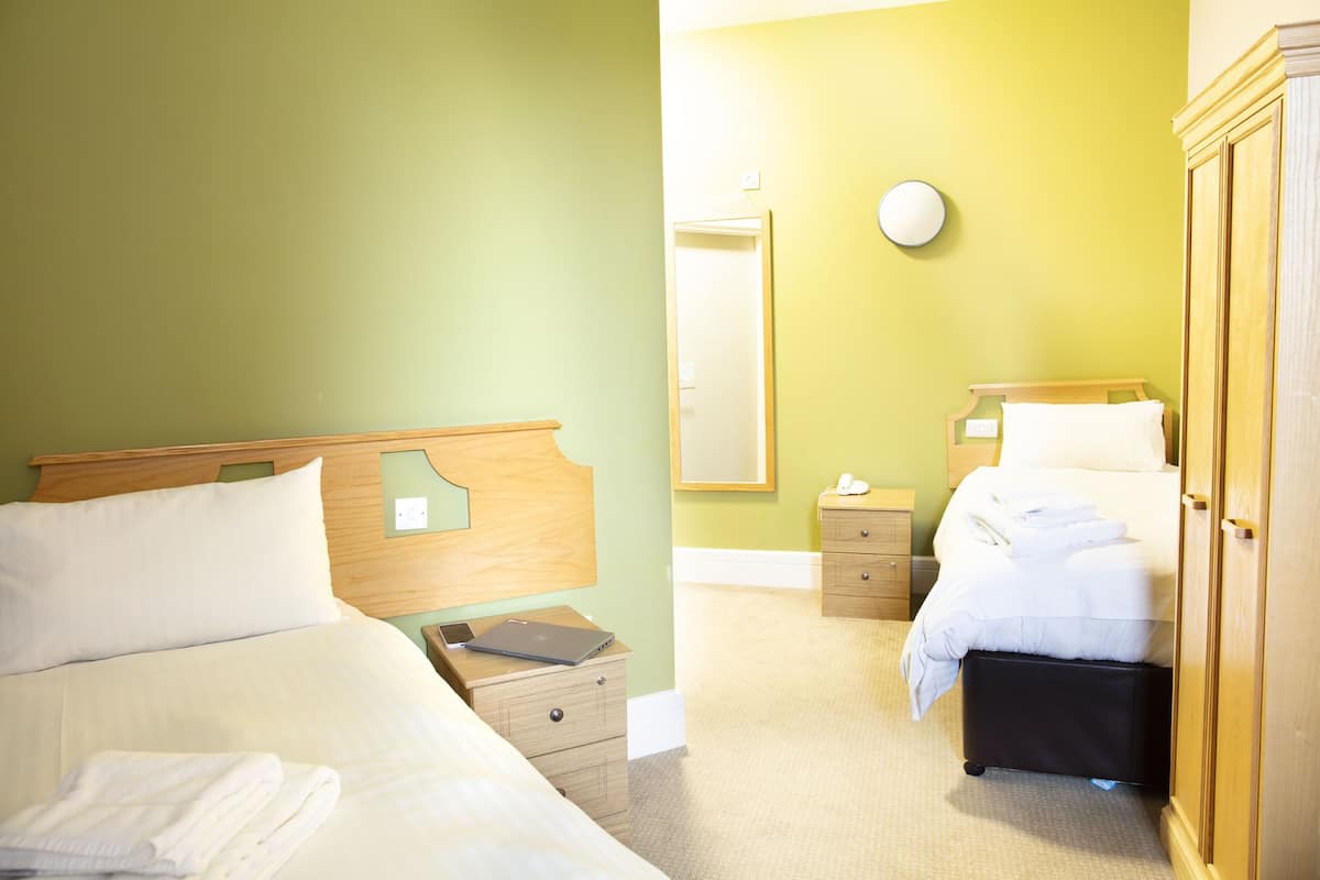 Une chambre d’hôtel avec deux lits, une armoire en bois, une table de chevet avec une lampe et un miroir au mur.
