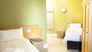 A hotel room with two beds, a wooden wardrobe, a bedside table with a lamp, and a mirror on the wall.
