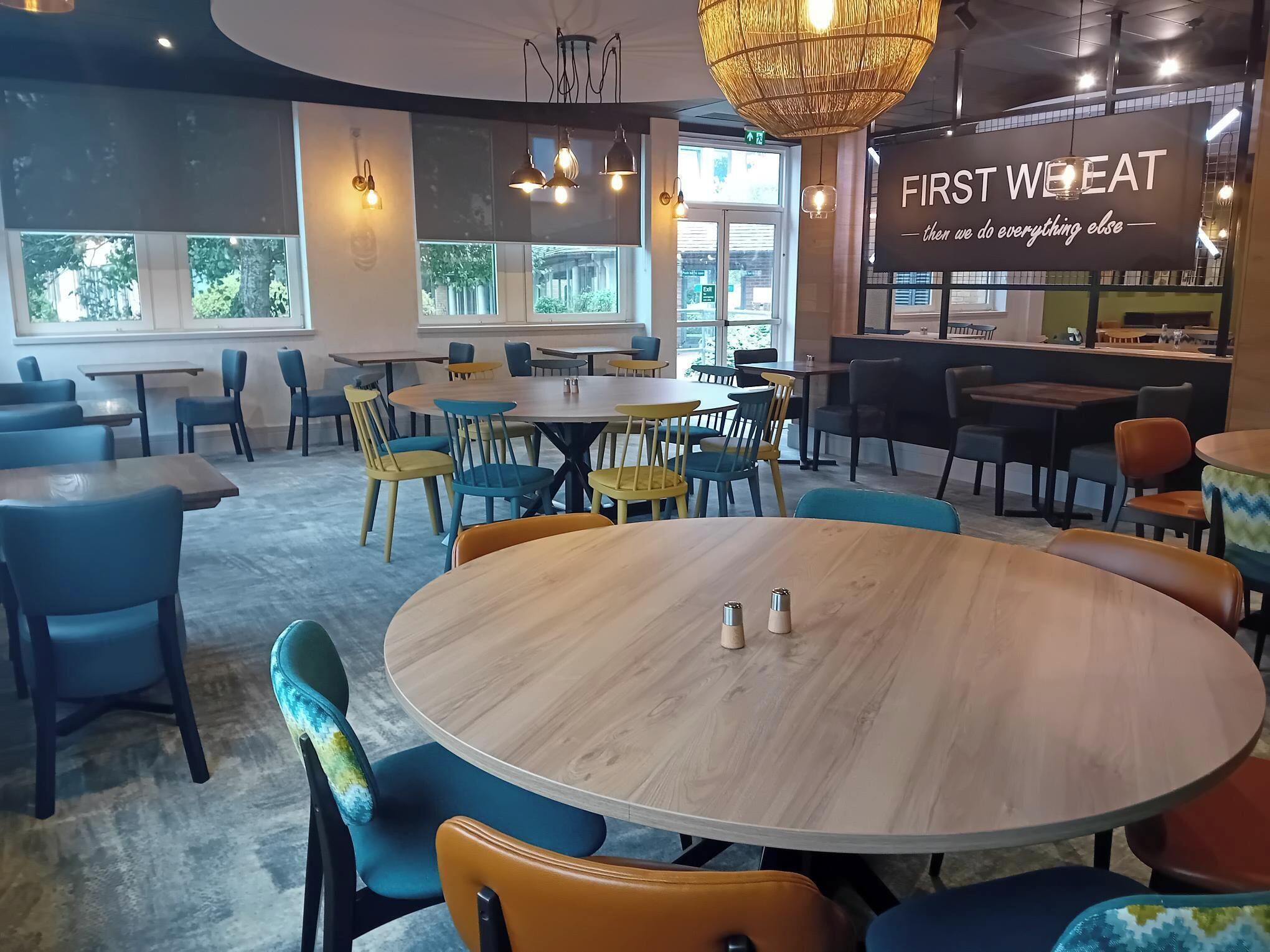 A modern dining area with round tables and chairs, large windows, and a sign reading "FIRST WHEAT".