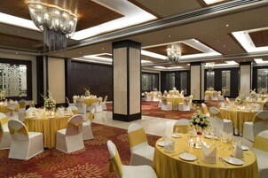Un salón de banquetes con mesas redondas, sillas blancas y detalles dorados.