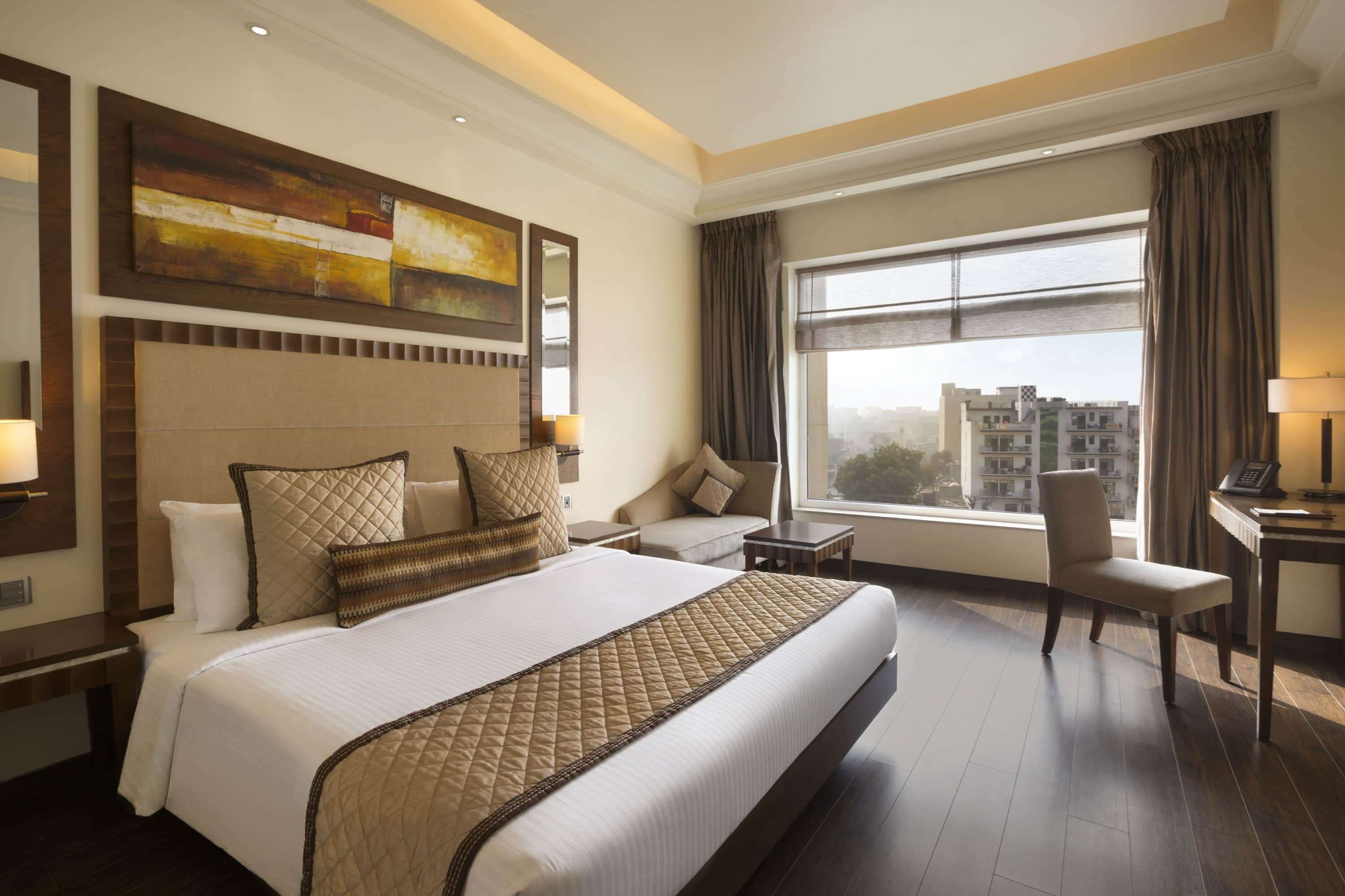 Quarto de hotel espaçoso, com uma cama grande, escrivaninha, cadeira e vista para a cidade através de uma janela ampla.