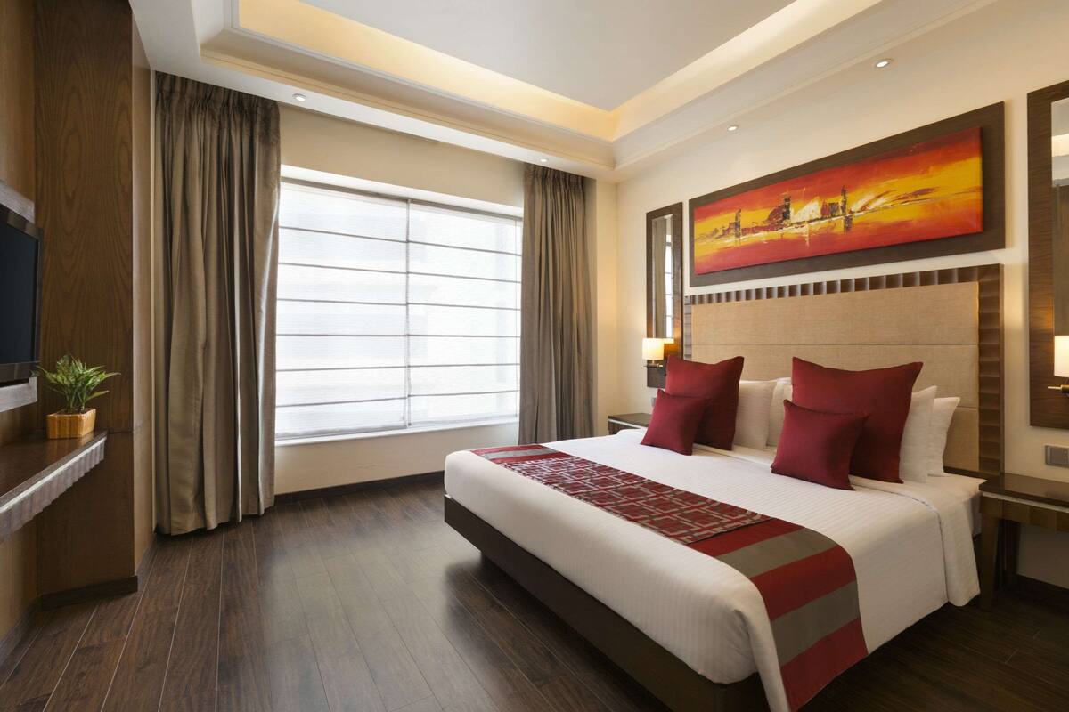 A hotel room with a large bed, a TV, a desk, and a window with curtains.