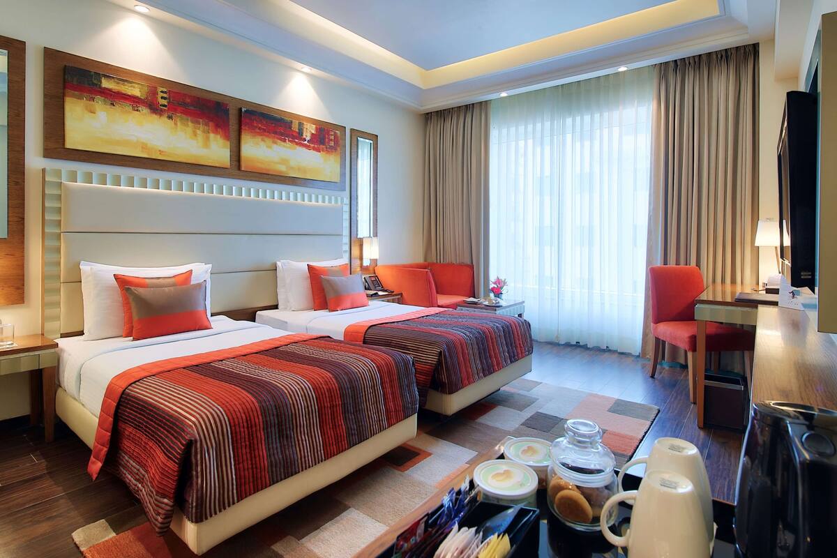 A hotel room with two beds, a desk, a chair, and a TV.