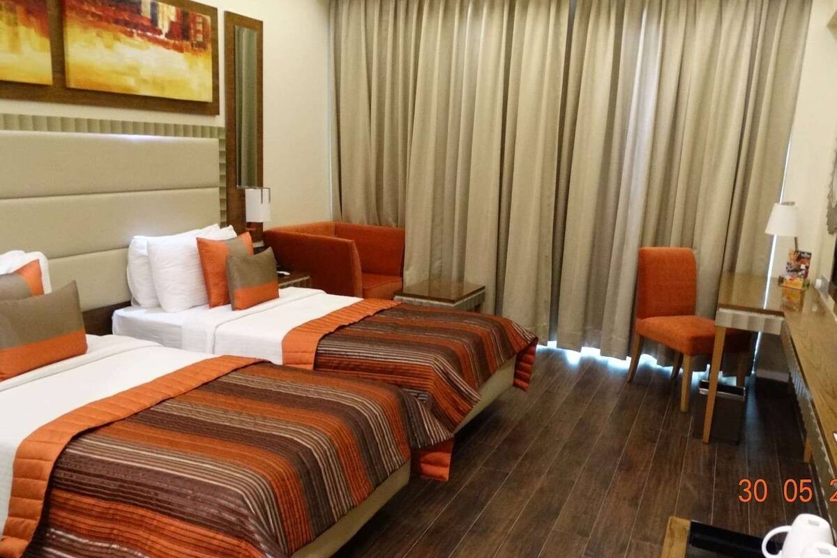 A hotel room with two beds, a desk, a chair, and a large window with curtains.