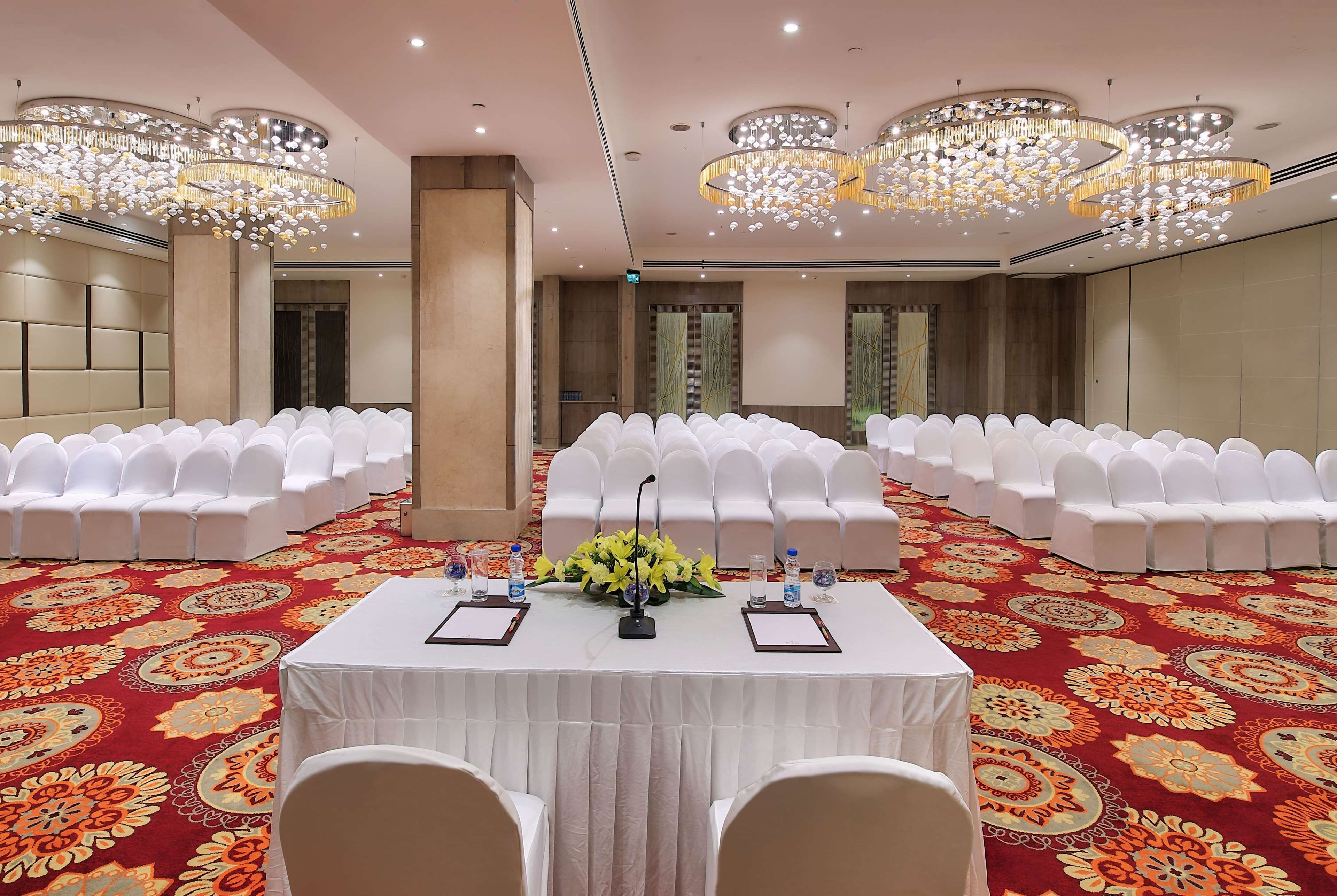 A conference room with rows of white chairs, a table with water bottles and notepads, and a floral centerpiece.