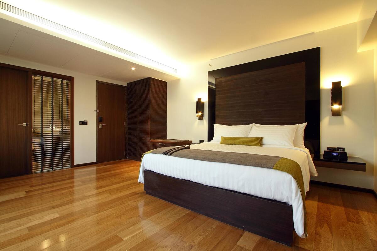 A modern bedroom with a large bed, wooden flooring, and built-in lighting.