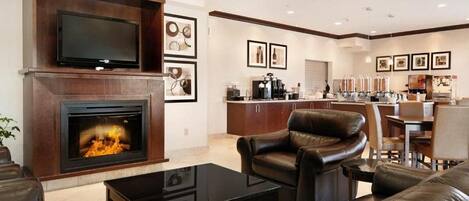 A modern living room with a fireplace, leather furniture, a flat-screen TV, and a kitchen area with bar stools and a coffee station.